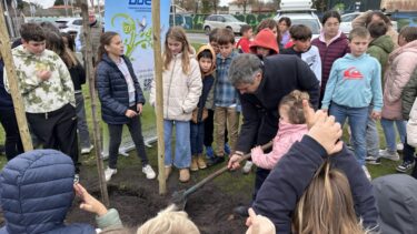 Le maire d'Arès plante un arbre. Il tient une pelle dans la main. Il est entouré d'enfants.