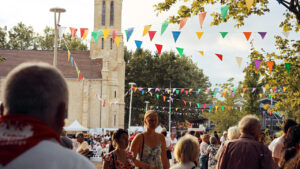 Place du Village d'Audenge à l'occasion de l'Autre Marché : des personnes avec des bandeaux rouges sont au premier plan et l'église en second plan