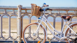 Vélo blanc avec un panier, posé contre une rambarde devant la plage