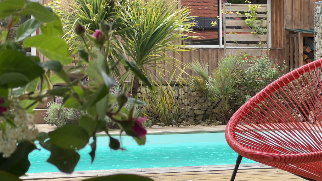 gite de france - bord de piscine et fauteuil rouge et plantes évoquant les vacances