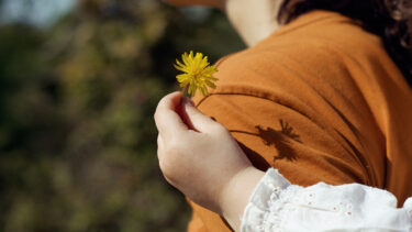 Main d'une petite fille derrière sa maman, tenant une petite fleur jaune