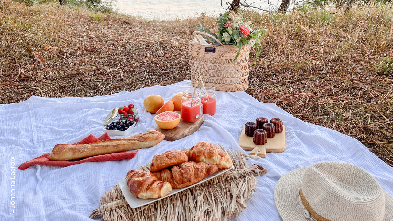Pique nique sucré avec des jus de fruit, canelés, viennoiserie et un panier en fond