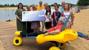 personnes debout qui tiennent un grand chèque placées devant un tiralo sur la plage du teich à l'occasion de l'inauguration du tapis de plage