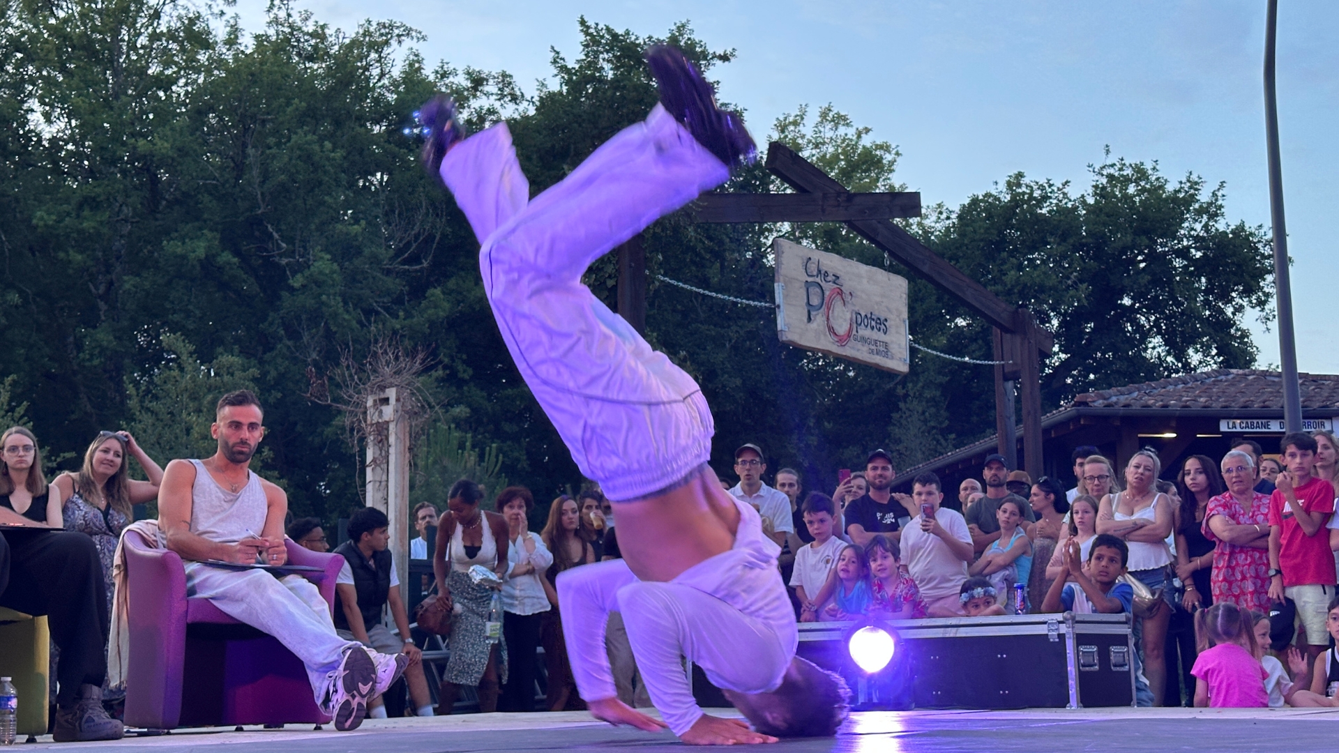 jeune homme qui fait une figure de breakdance sur une scène devant des dizaines de personnes