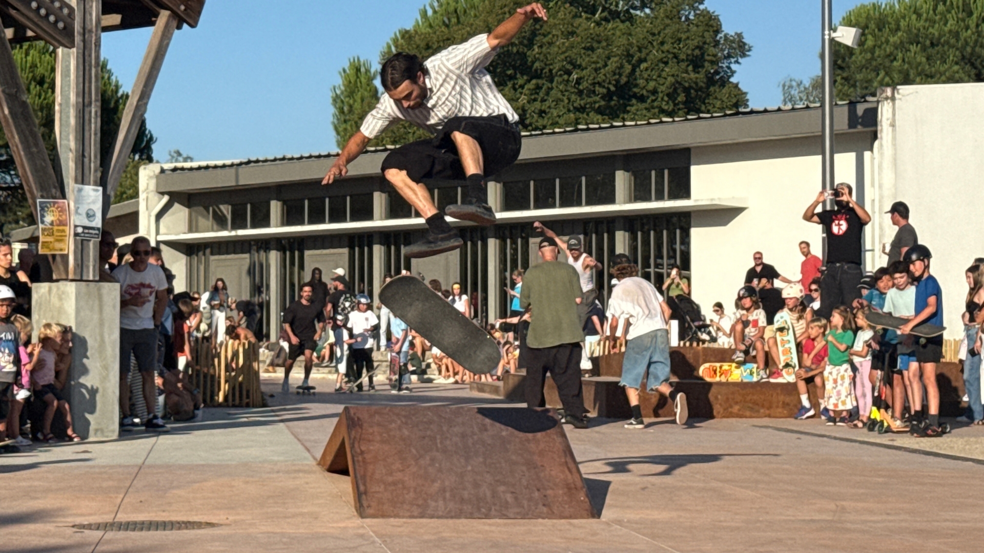 homme qui effectue une figure en skate, une foule de personne le regardent depuis la place dominique mayonnade à mios