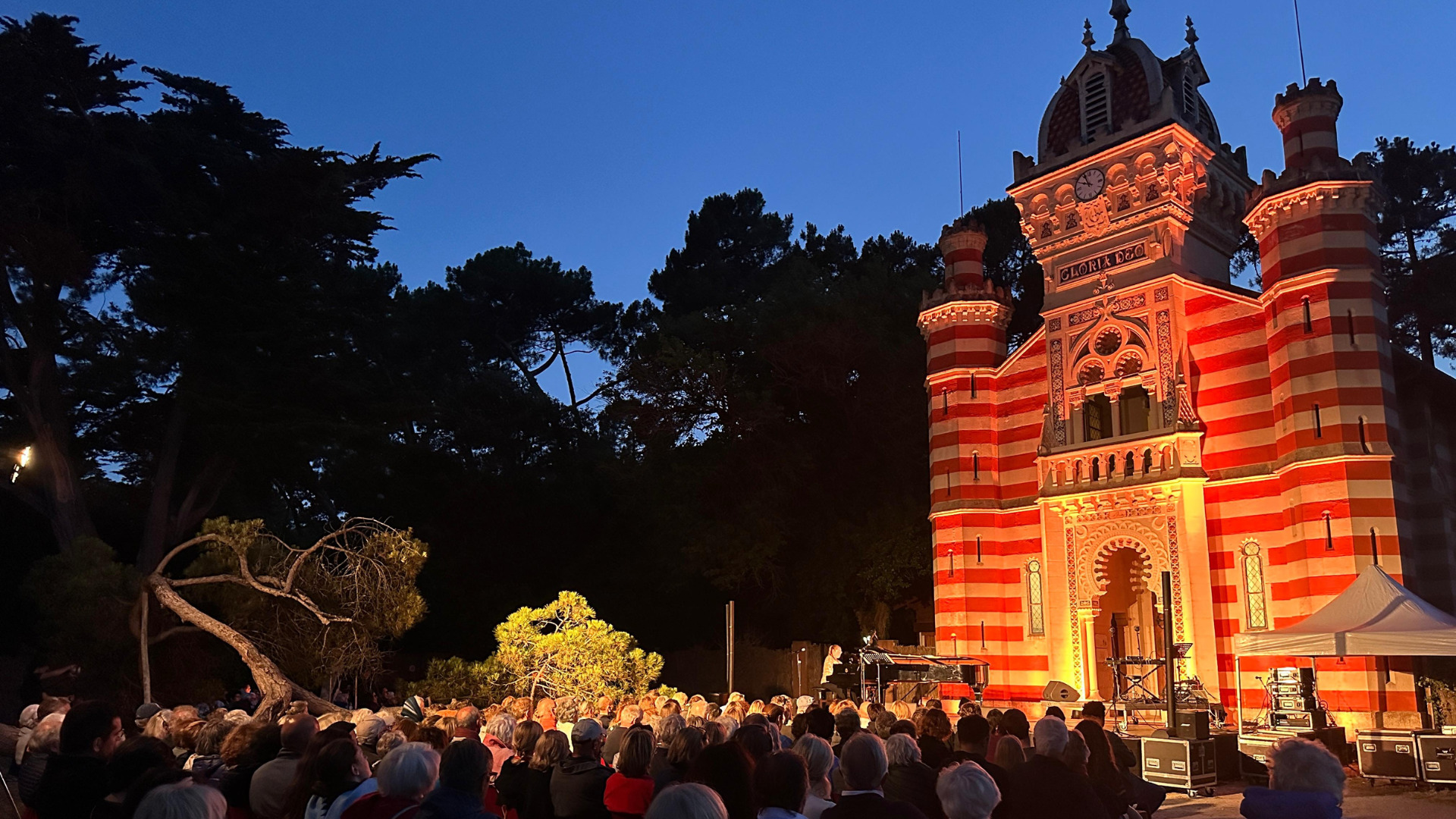 parvis de la chapelle de l'Herbe à Lège Cap Ferret à la nuit tombante. des musiciens jouent devant une foule de personne