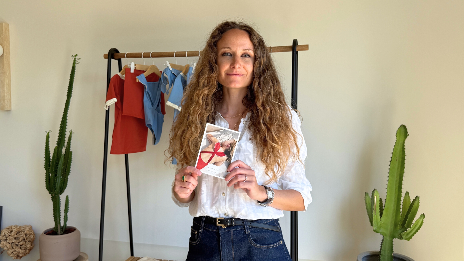 Photo portrait de Morgane Maillet Chaubaud, fondatrice de la marque de maillots de bain A thing for me.(femme qui tient une carte postale dans les mains type flyer avec des maillots de bain pour enfant colorés en arrière plan fabriqués à partir de filets de pêche)