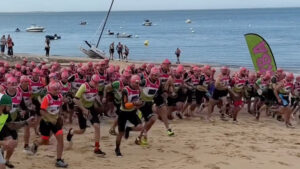 Un groupe de coureur avec des bonnets de bains roses s'élance sur la plage