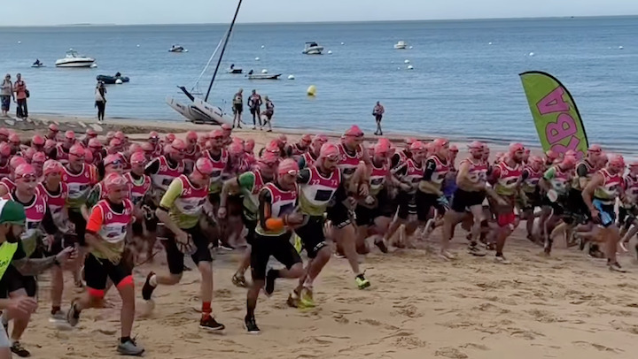 Un groupe de coureur avec des bonnets de bains roses s'élance sur la plage