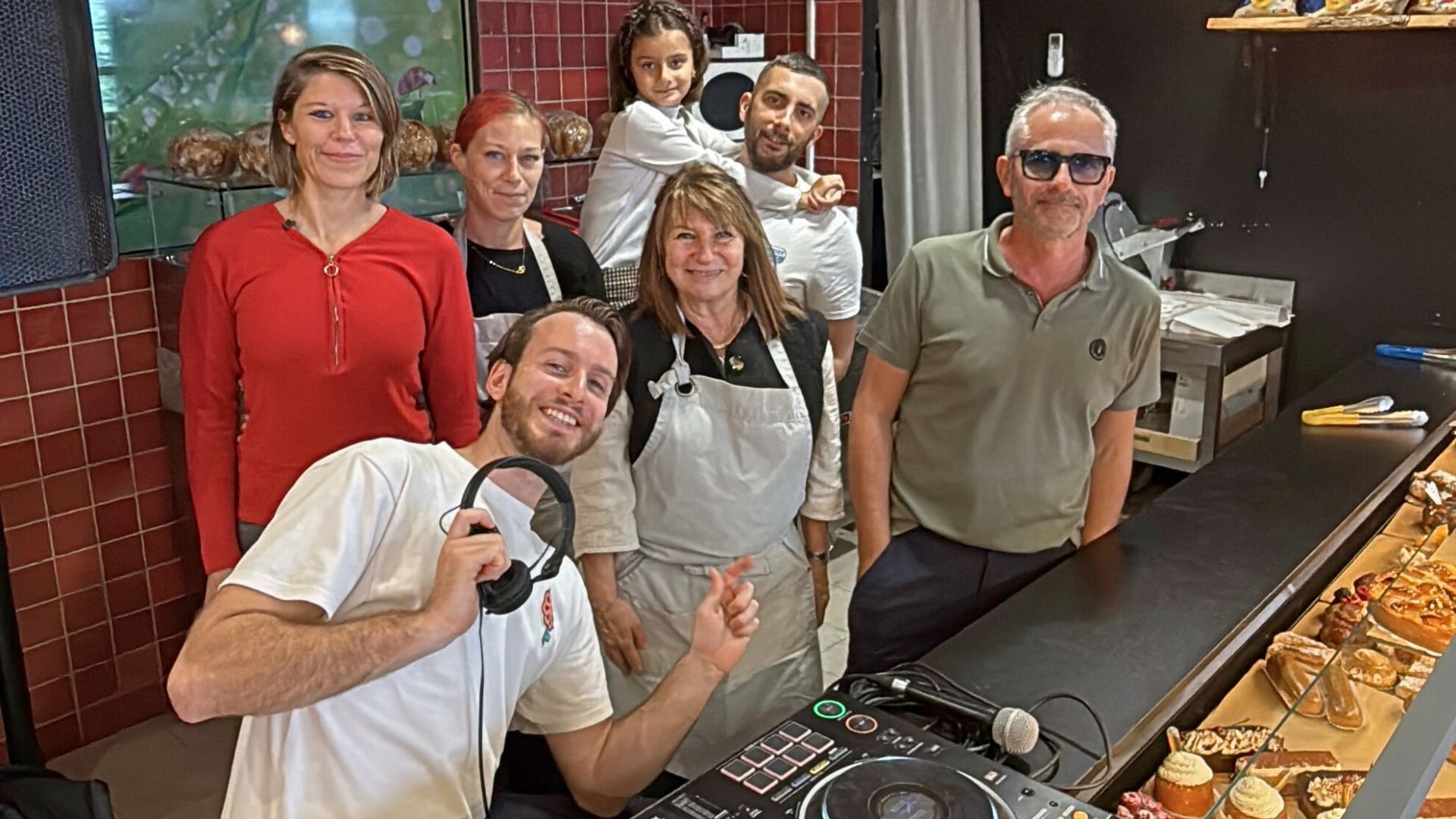 Un homme avec un casque de DJ entouré de 6 personnes au comptoir d'une boulangerie