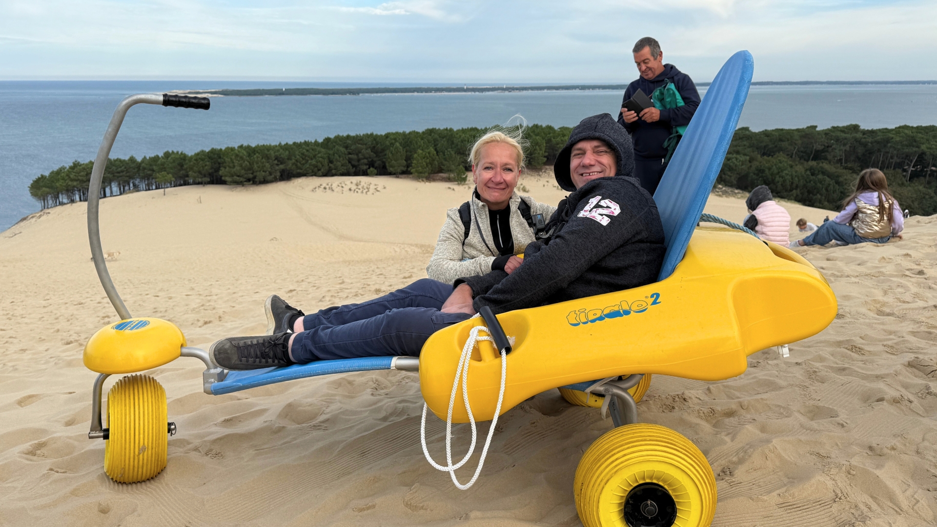 opération handi dune : un homme en situation de hancap dans un tiralo au sommet de la dune du pilat avec sa femme à côté de lui