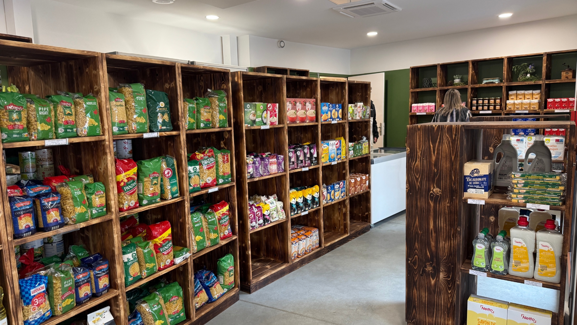 intérieur de l'épicerie sociale et solidaire de Biganos au sein de la maison solidaire : des étagères en bois fumé et des produits alimentaires dessus