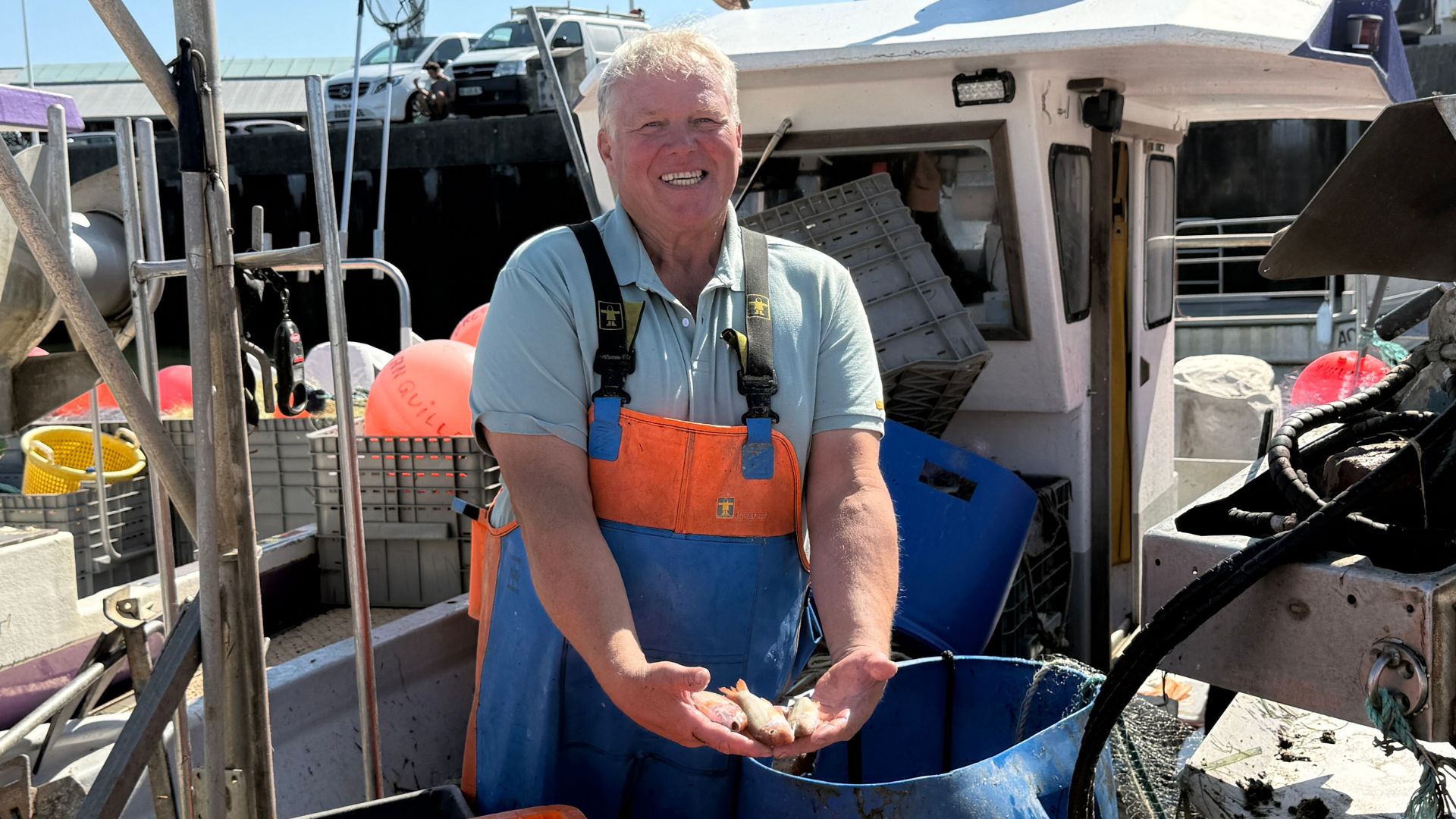 Un pêcheur tient des petits poissons dans ses mans sur son bâteau.