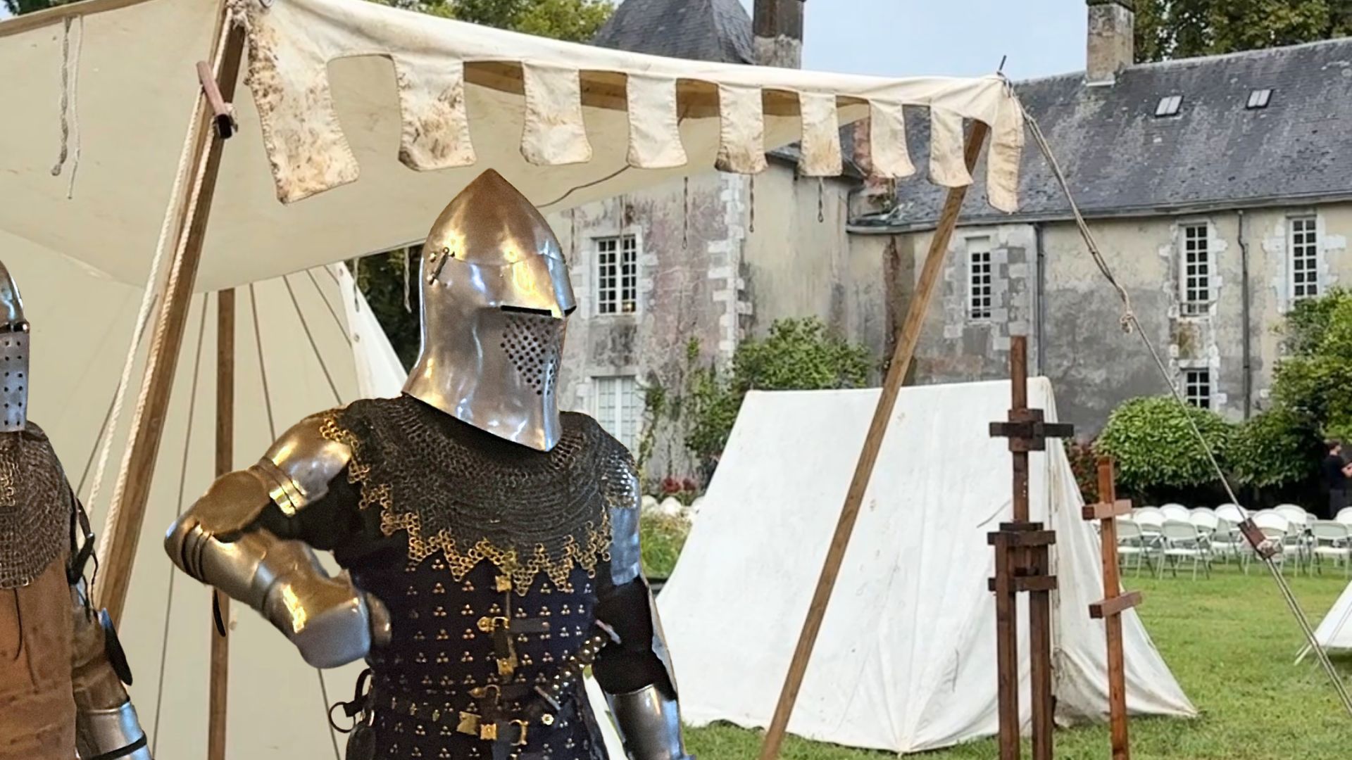 Un chevalier en armure devant des tentes médiévales. Un chateau en arrière plan.