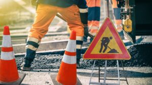 plot et panneaux de chantier sur une route. PIed d'un ouvriers habillé en orange.