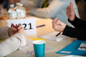 deux personnes discutent à une table. on ne voit que leurs mains, des carnets, des stylos et des gobelets