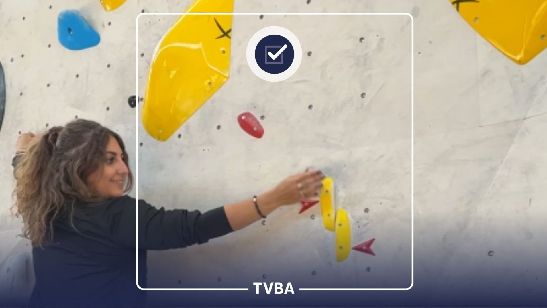 Une jeune femme habillée en noir sur un mur d'escalade avec de sprises de toutes les couleurs