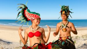 deux danseurs polynésiens en tenue traditionnelle devant une plage