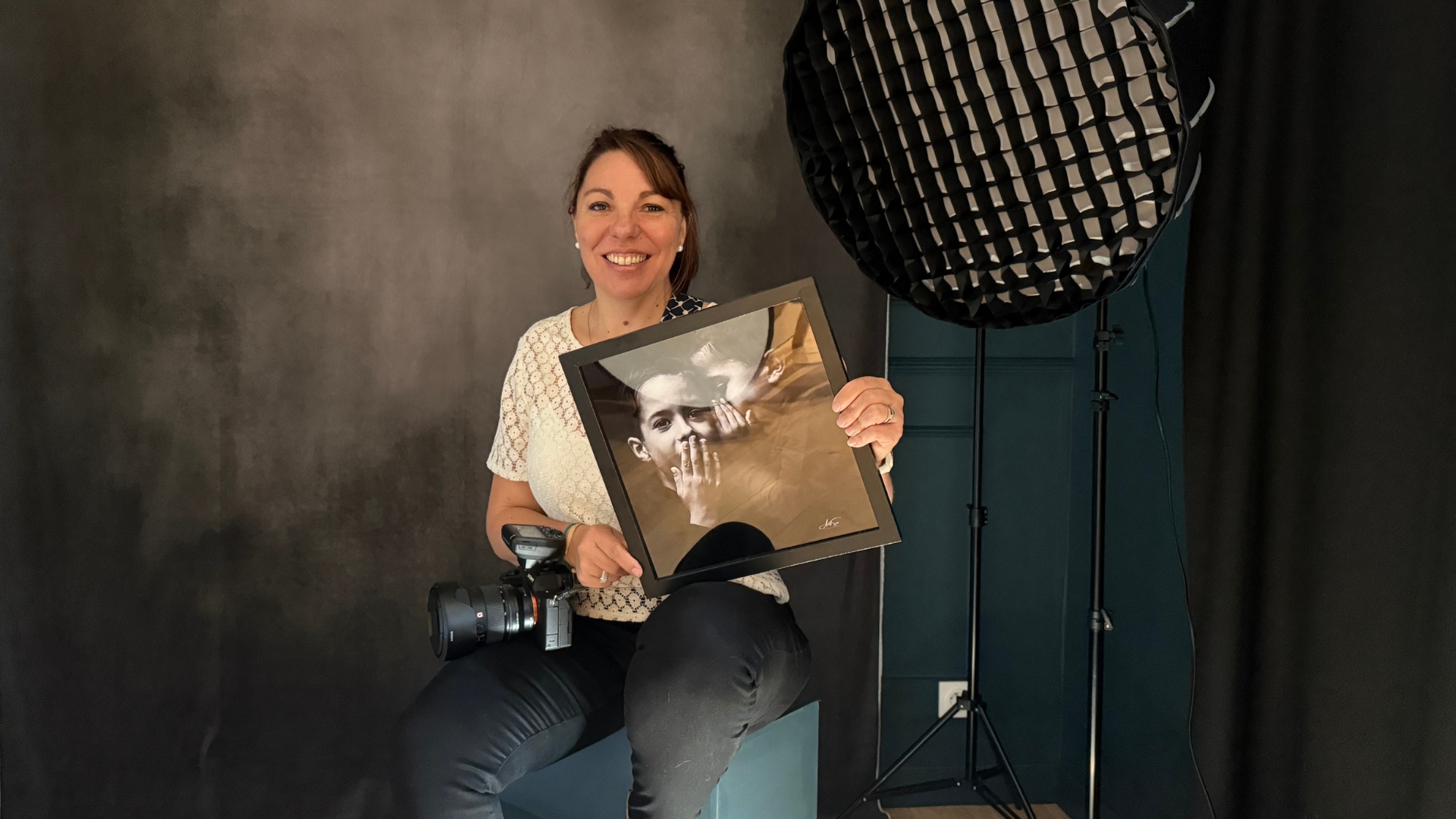 portrait d'une portraitiste : femme qui tient un cadre photo dans les mains et porte un appareil photo autour du cou dans un studio photo