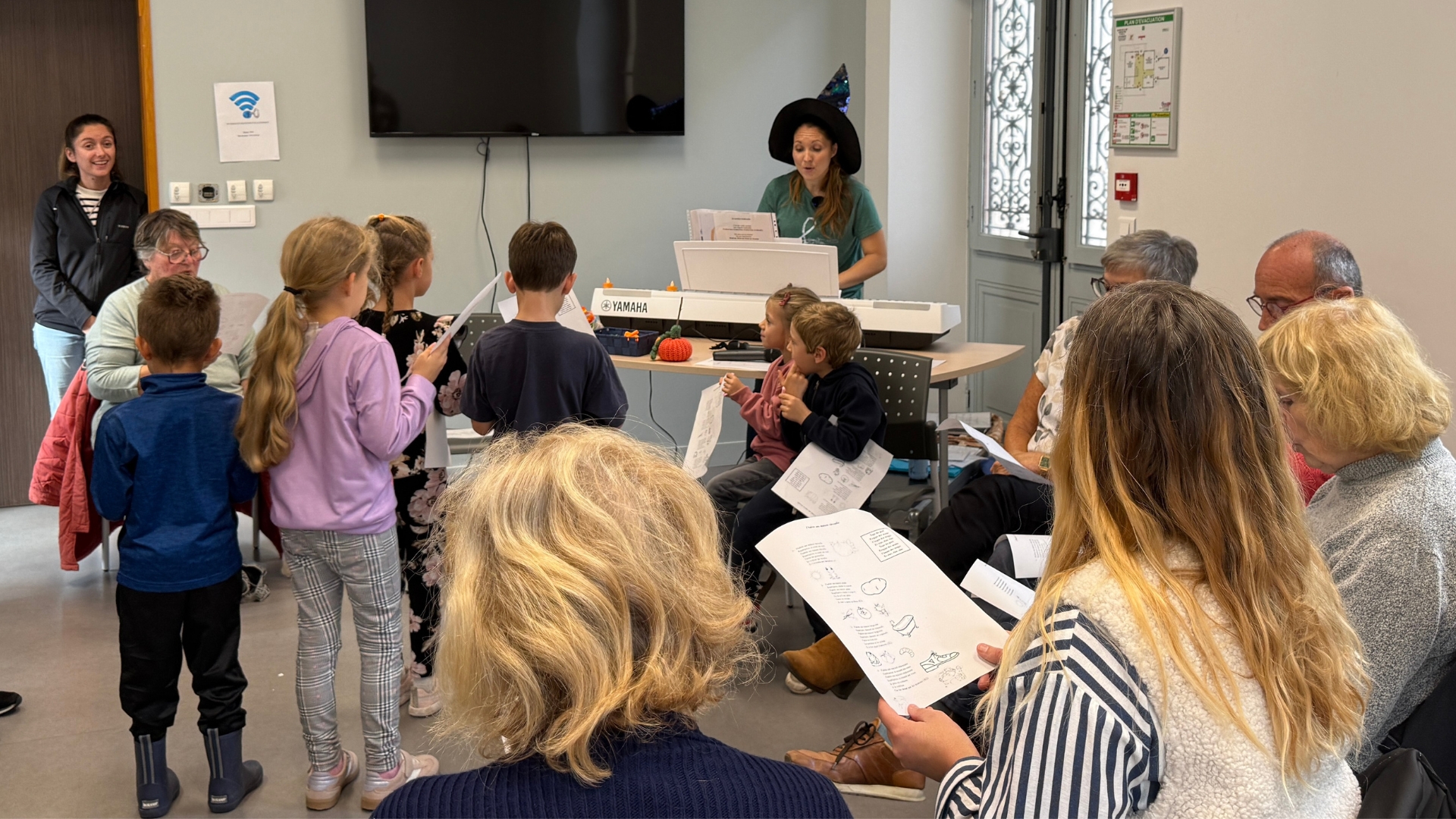 atelier de musicothérapie à audenge : des jeunes enfants debout et des séniors assis dans une salle avec une femme qui joue du piano
