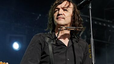 chanteur aux cheveux longs et en chemise noir sur scène