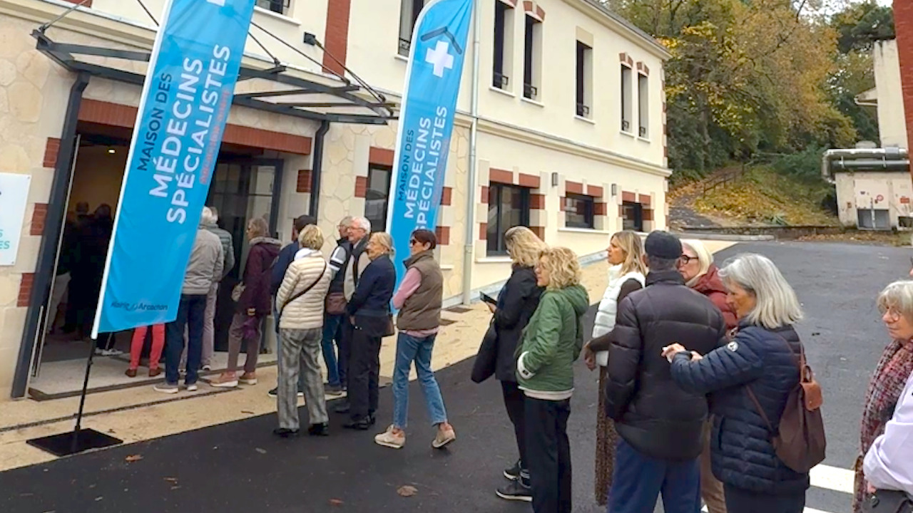 File d'attente devant la maison des spécialistes d'arcachon (batiment beige et oriflammes bleus