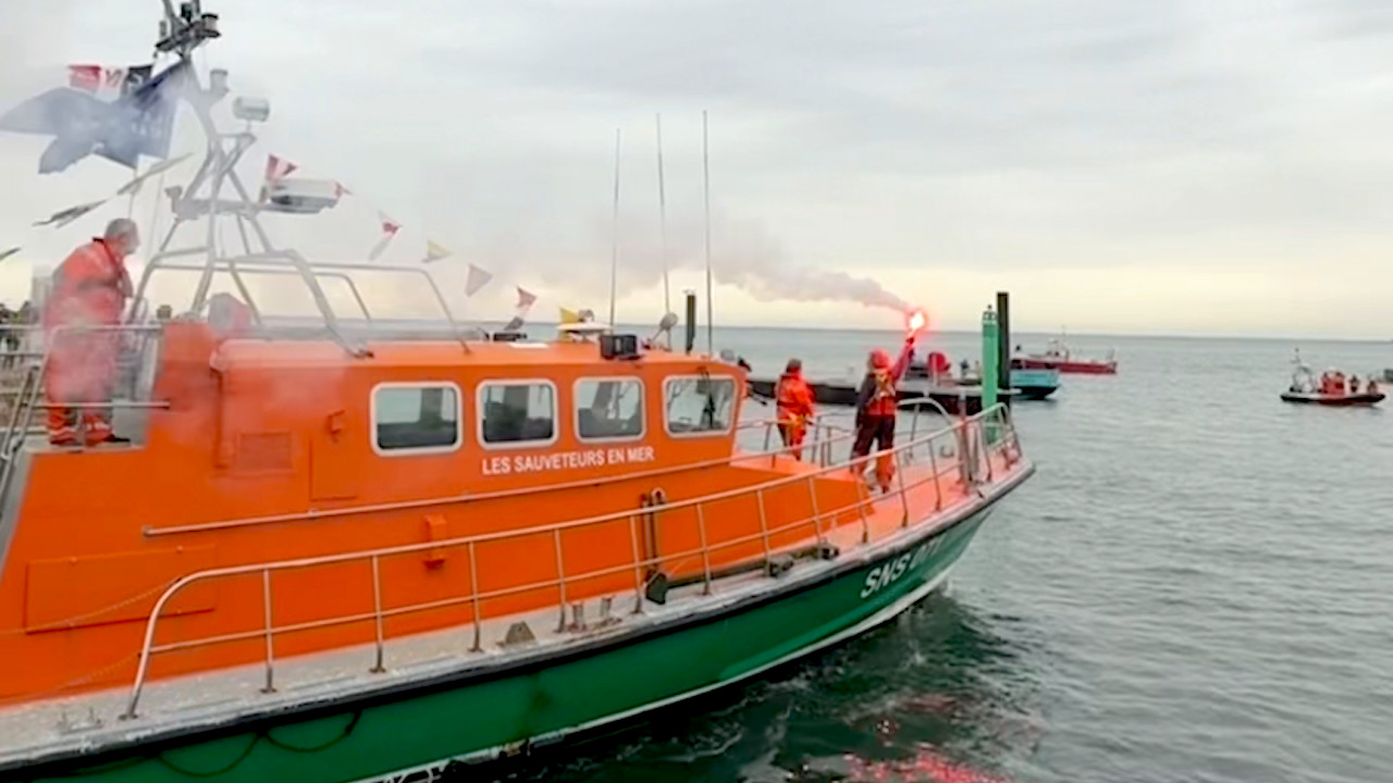 Un gros bateau orange et vert, sur le pont un homme tient un fumigène.