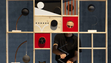 un artiste caché derrière son oeuvre d'art en bois : étagères rouges et beiges