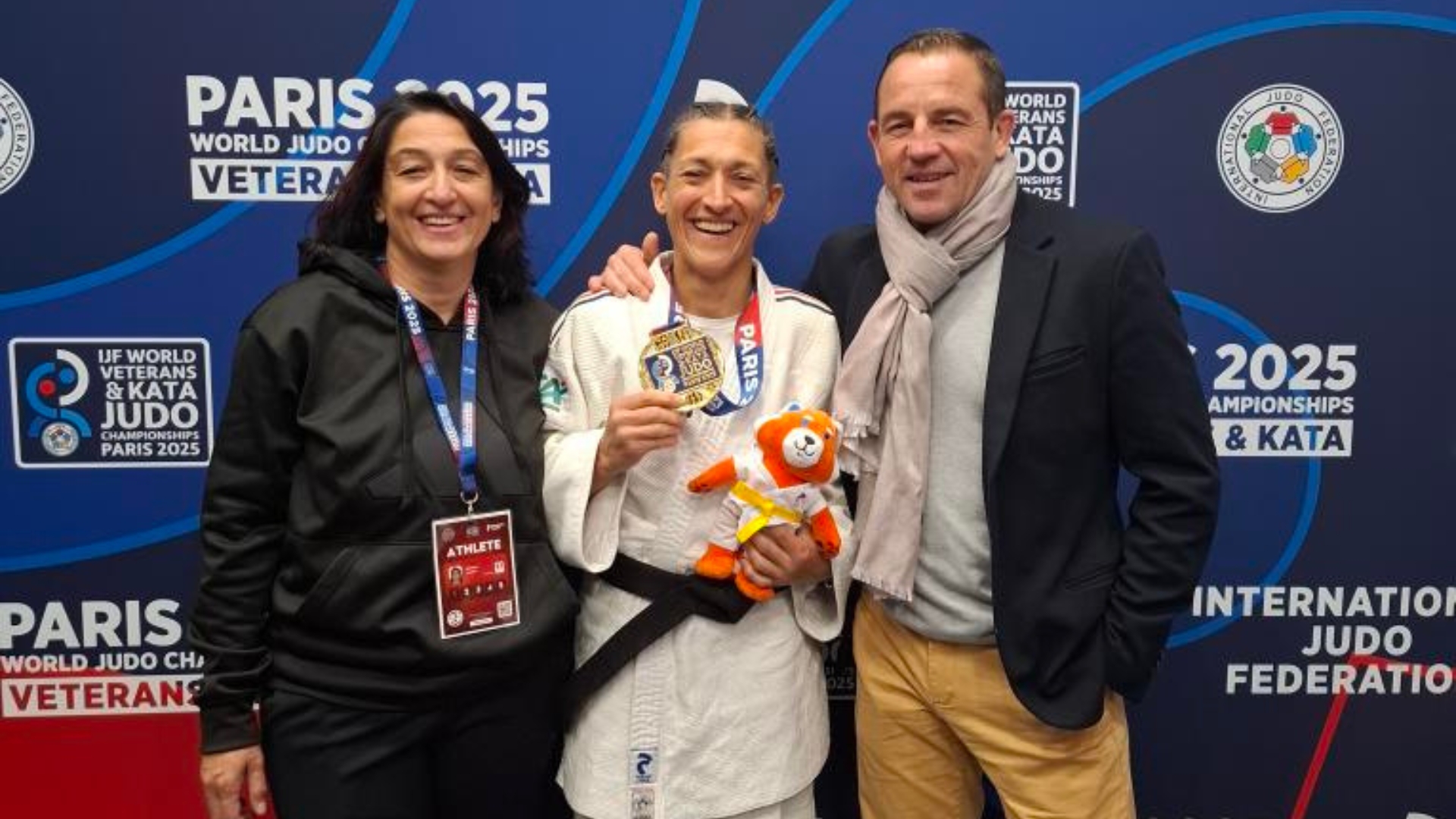frédérique stoezel, championne du monde de judo en tenue avec sa médaille, son entraineur à ses côtés et une autre licenciée du club à sa droite.