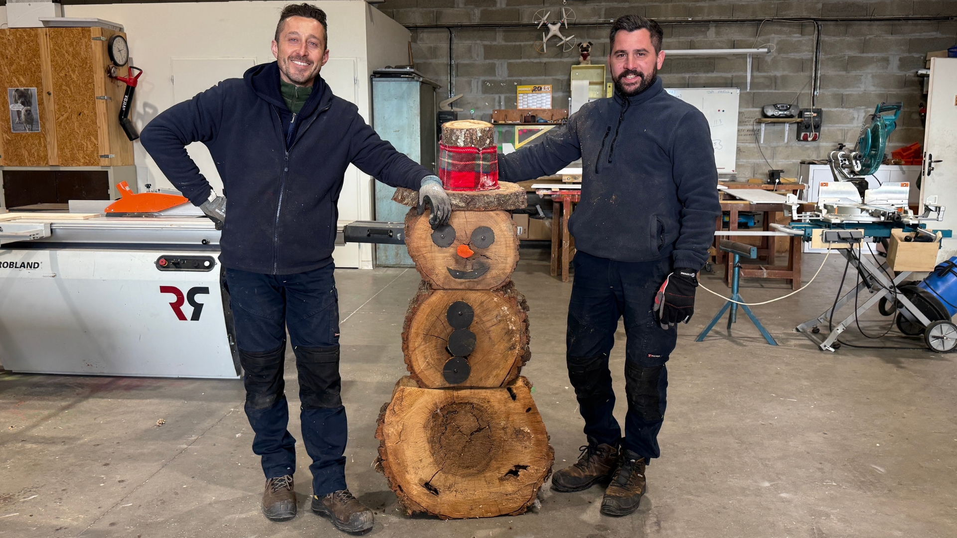 deux hommes avec un bonhomme de neige en bois au centre dans l'atelier des services techniques du Teich à l'approche de Noël