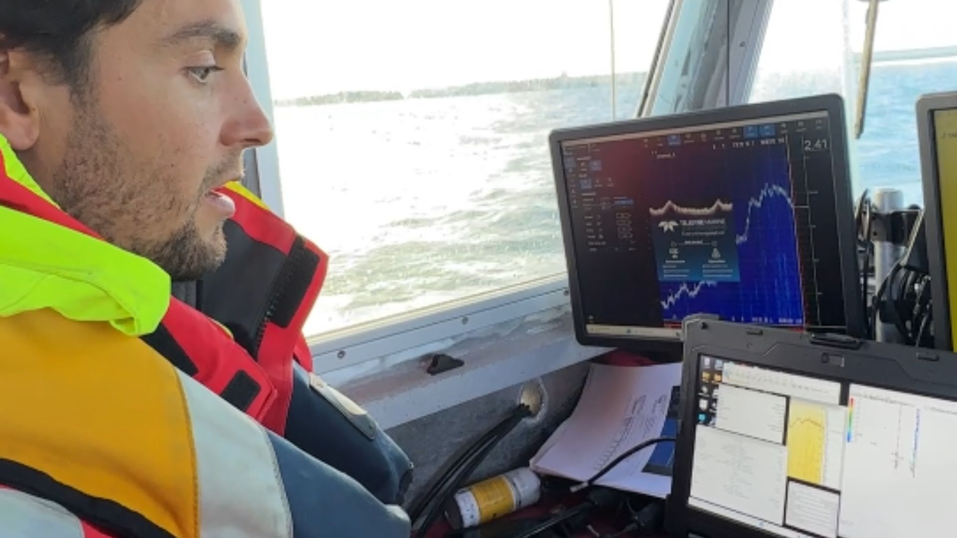 un homme avec un gilet de sauvetage dans un bateau et devant des écrans