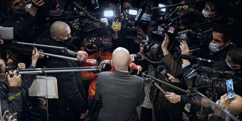 un homme chauve dans le noir face à de très nombreux micros