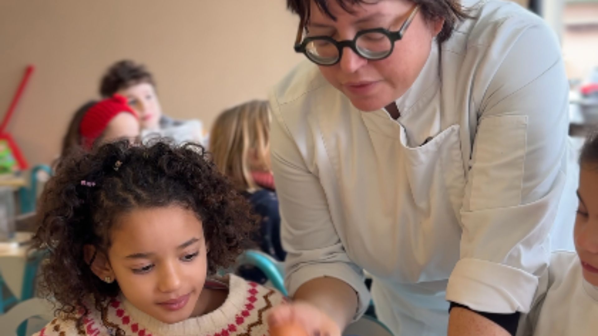 Une cheffe de cuisine accompagne une petite fille dans la réalisation d'une recette