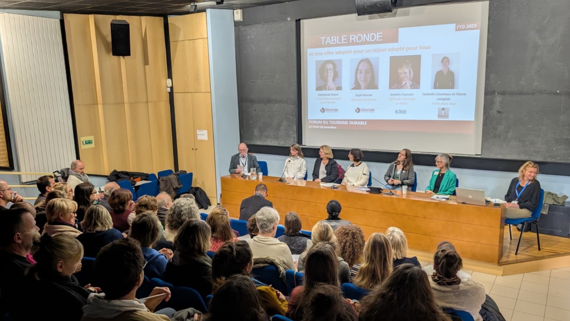 une centaine de personnes assises dans la salle multimédia du Teich pour le forum du tourisme durable. 7 personnes sont assises sur la tribune sur la scène avec un powerpoint en arrière plan