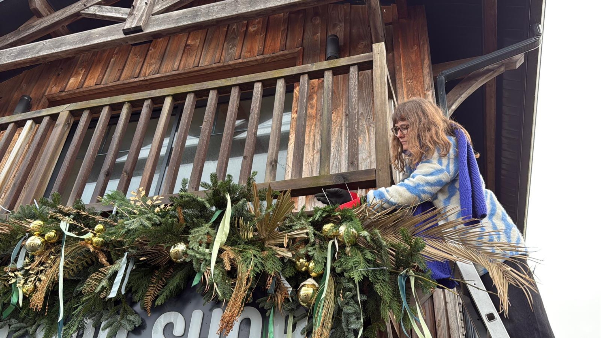 léa, jeune femme artiste florale sur une échelle devant une boutique en train de réaliser une composition florale à base de sapin, de palmiers pour Noël