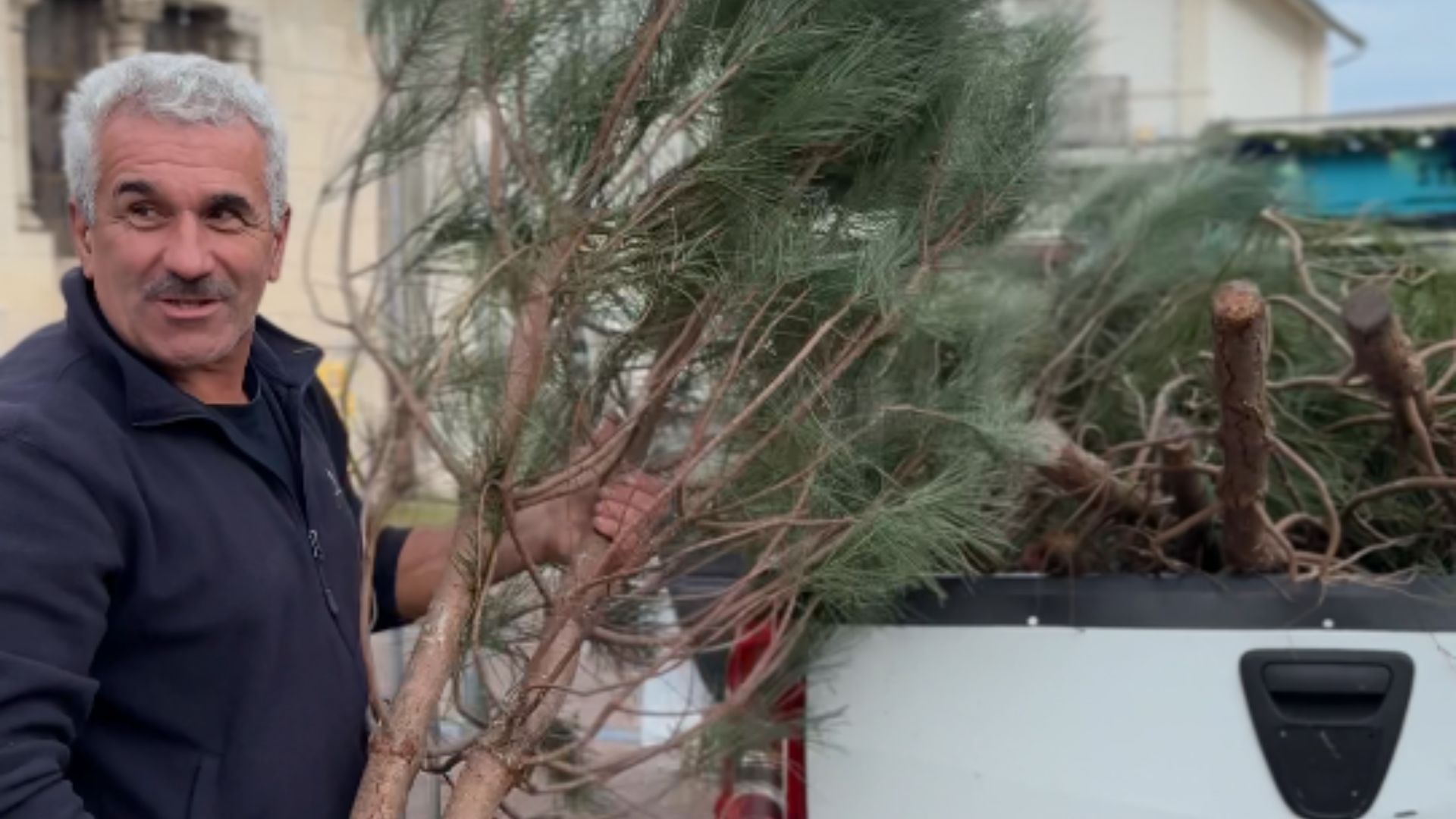 Un homme moustachu tient un pin dans ses bras devant une voiture blanche