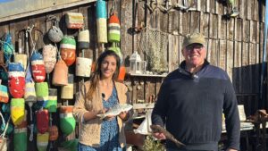 Un homme et une femme tiennent des poissons dans leur main devant une cabane en bois