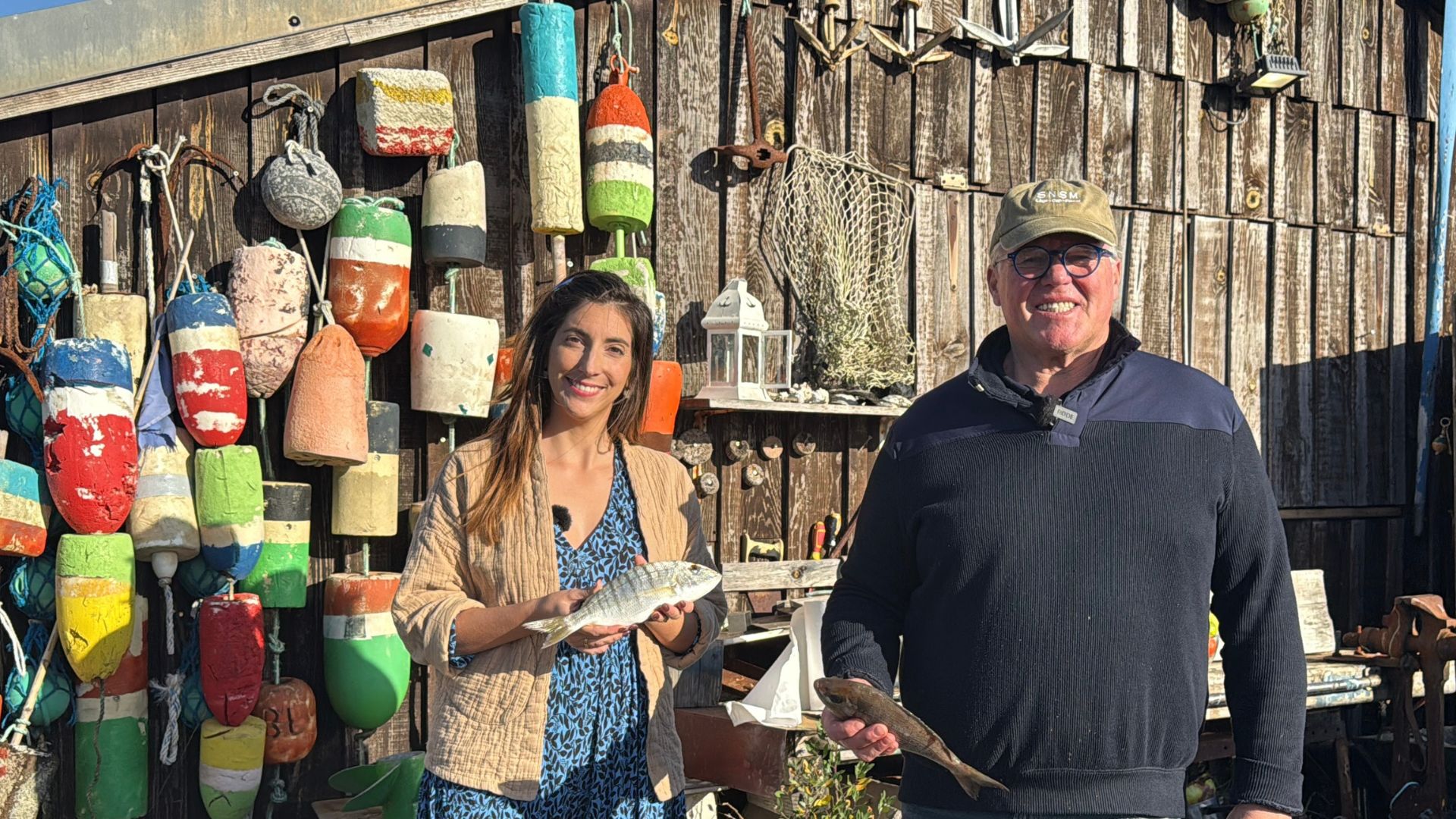 Un homme et une femme tiennent des poissons dans leur main devant une cabane en bois