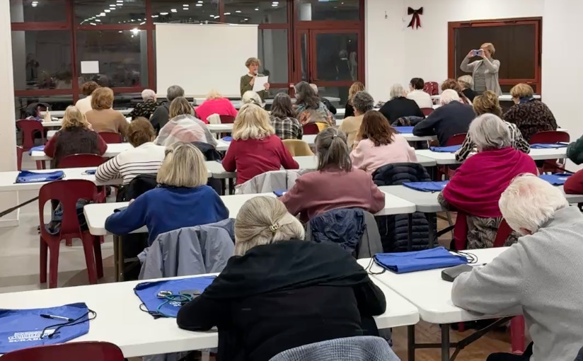 un groupe de personnes assises de dos mendant qu'une dame au fond de la salle dicte un texte