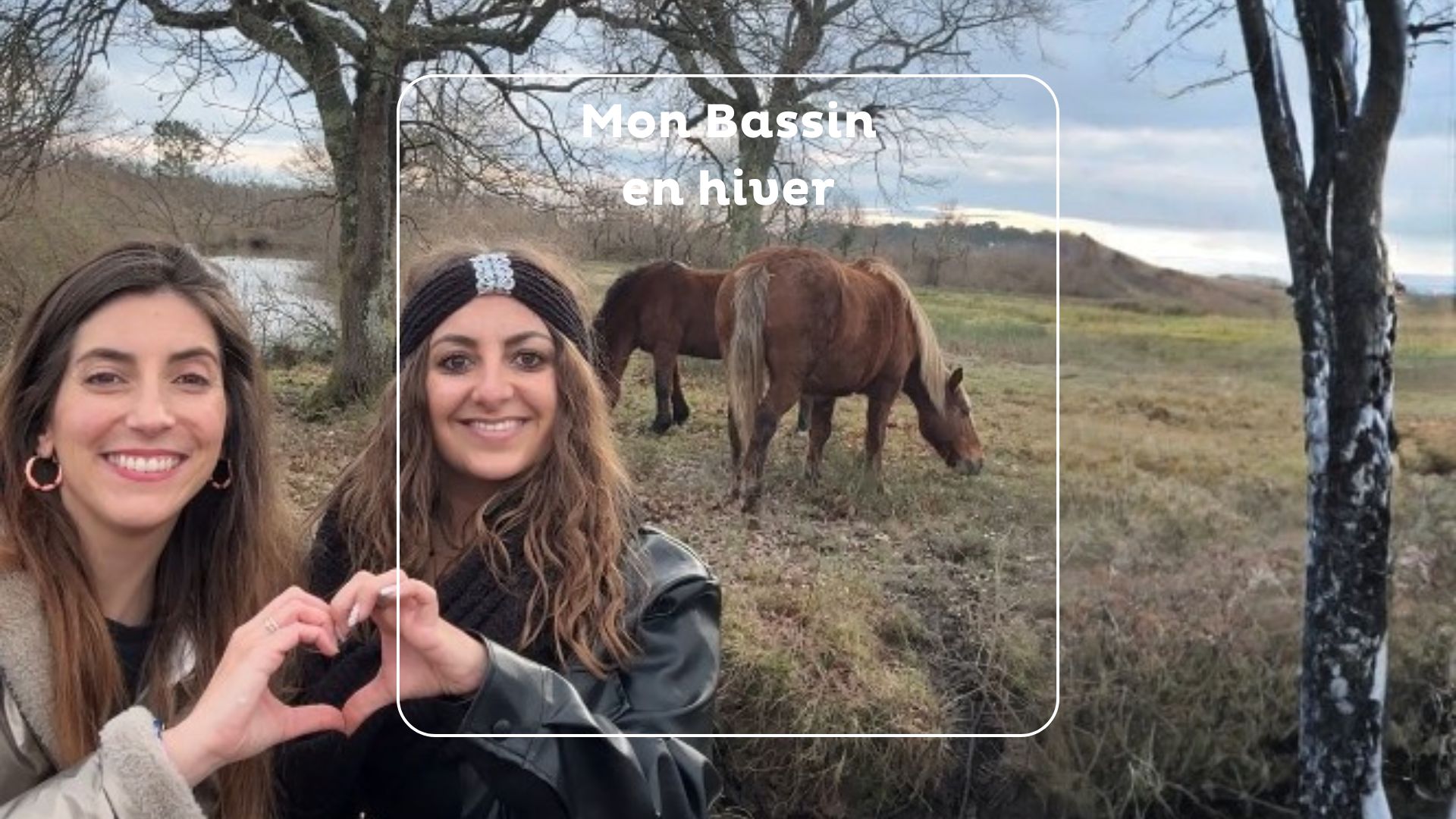 Deux jeunes femmes forment un coeur avec leurs mains, derrière des chevaux dans un près.