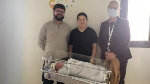 trois adultes debout derrière un landau avec un bébé dedans