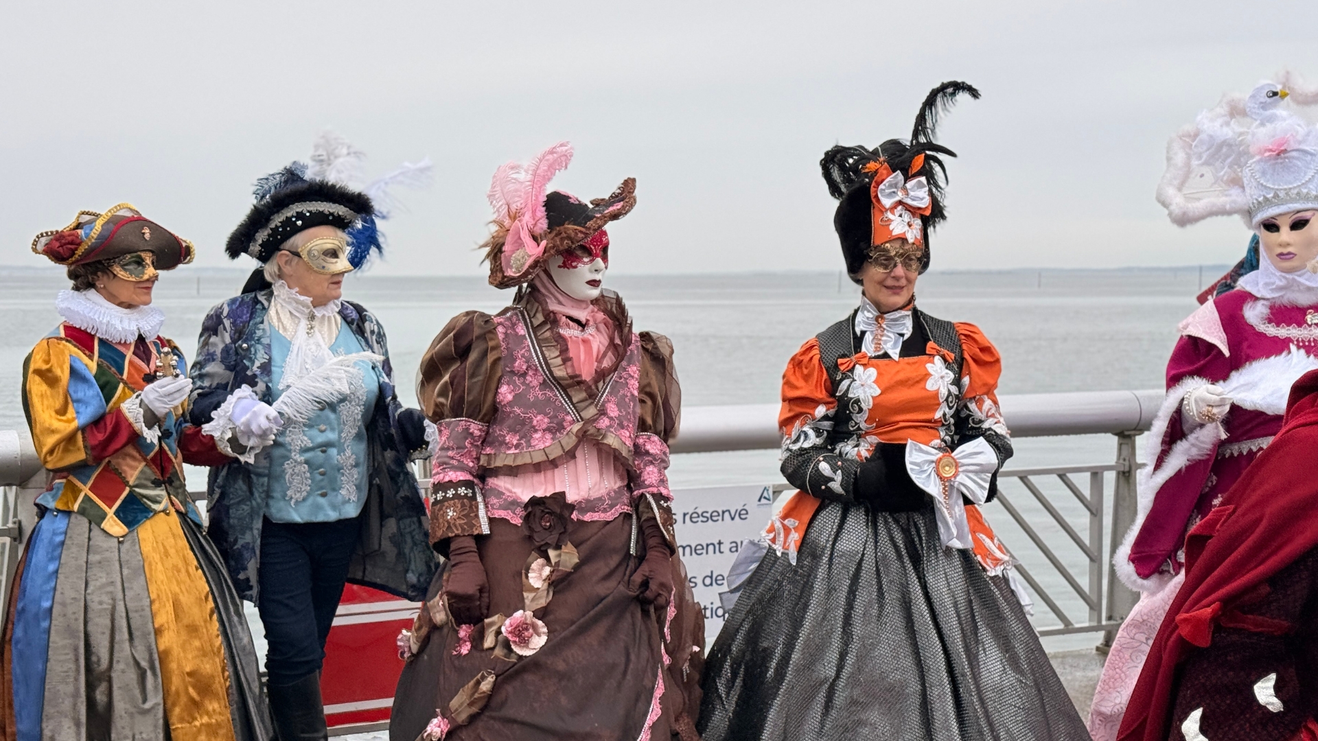 5 personnes habillées avec des costumes vénitiens et des masques, au bout de la jetée d'andernos sous un ciel gris à l'occasion de la fête de la befana