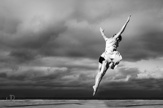 photo en noir et blanc d'une danseuse devant un ciel nuageux.