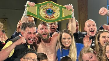Un homme tient un bouclier de boxe dans les mains. il est entouré d'une foule de personne