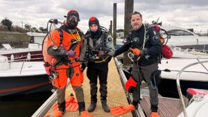 3 plongeurs en combinaison avec le matériel de plongée sur le dos debout, sur le ponton du port d'arcachon avec des bateaux en arrière plan