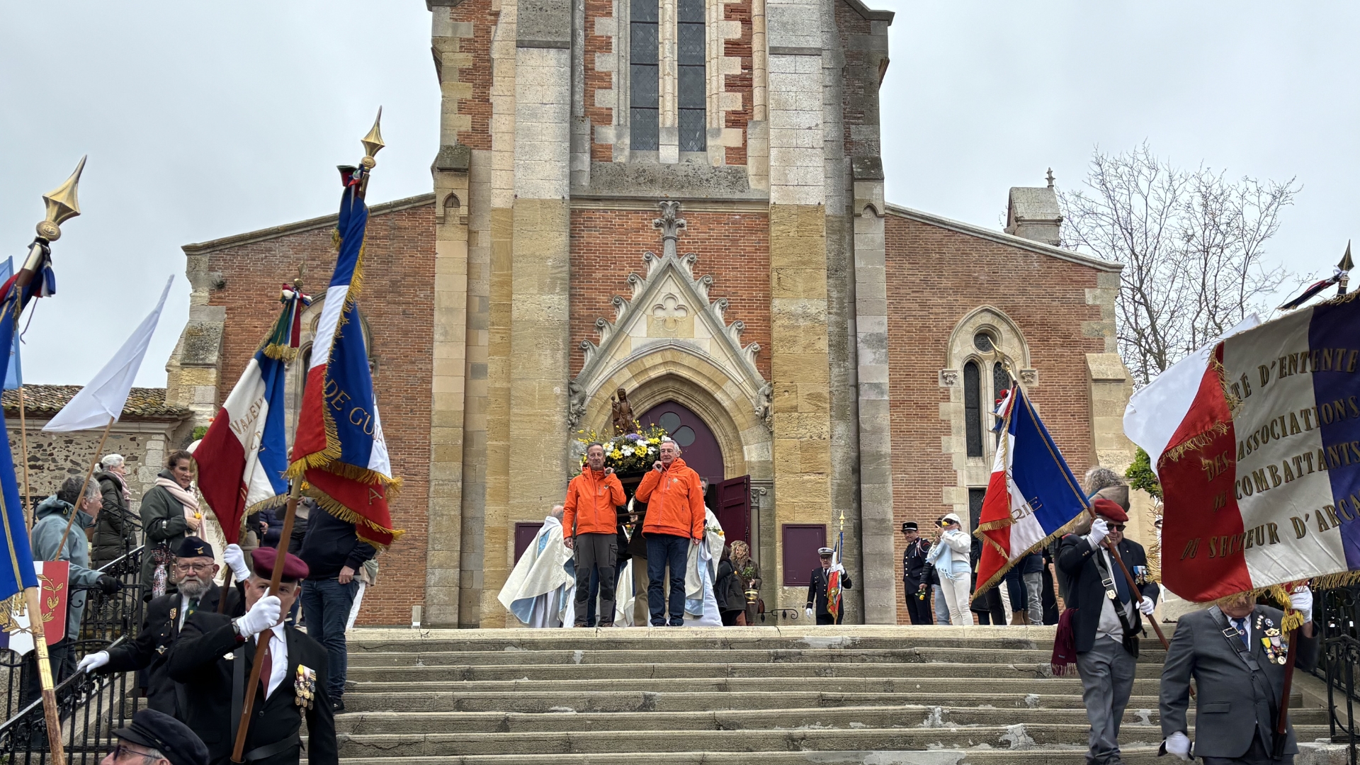 gerbe fleurie surmontée d'une vierge portée par des sauveteurs de la SNSM, des portes drapeaux et en arrière plan la basilique notre-dame d'Arcachon