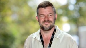 Eric Naulleau : un homme avec des cheveux brun une barbe grisonnante avec une chemise beige de face.