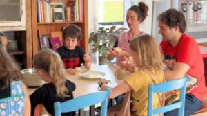 un gruope d'adultes et d'enfant autour d'une table, sur des chaises bleues : ils étalent de la pâte à crèpes marocaines
