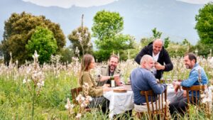 5 personnes assises à une table posées dans un champs de fleurs avec des montagnes en arrière-plan
