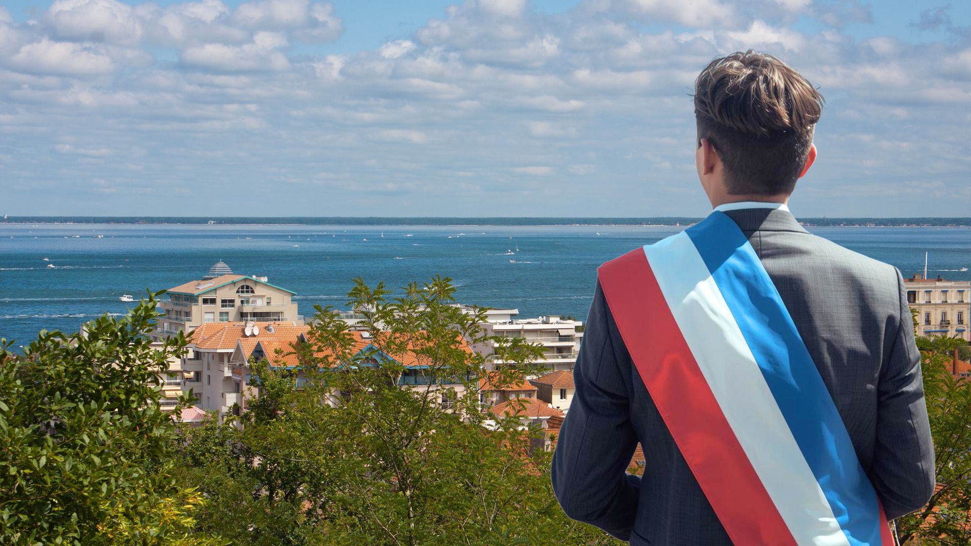 Une personne en costard et cheveux courts pose de dos avec une écharpe tricolore de maire. En arrière plan : une photo en hauteur de la ville d'Arcachon